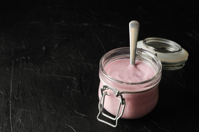 Glass jar with fruit yogurt on dark cement background, space for text