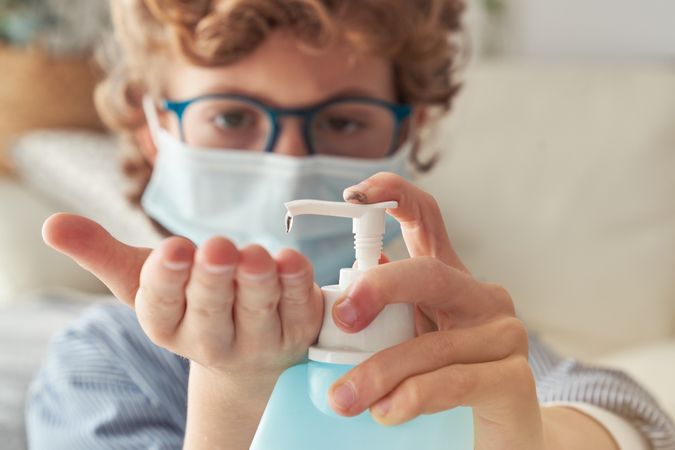 Crop boy in mask applying sanitizer on hand
