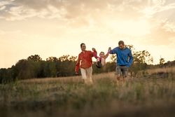 Happy family playing and swinging their daughter between them in a field at sunset.