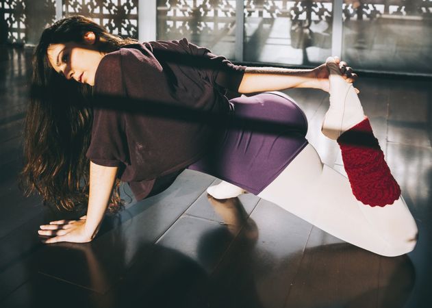 Ballerina dancer warming up flexible body in sunny studio.