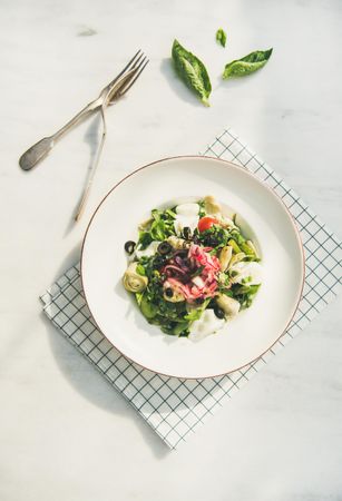 Artichoke salad in bowl, light background with checkered napkin, spinach vertical composition