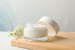 Jar with cream, allium flowers and board on blank background, copy space