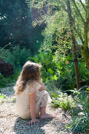 Profile of a young girl wearing a dress sits on a rock path in her garden