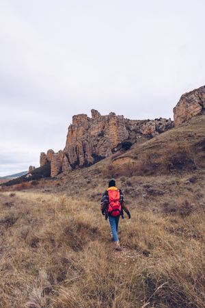 Hiker with backpack walking along rural road to cliff on gloomy day