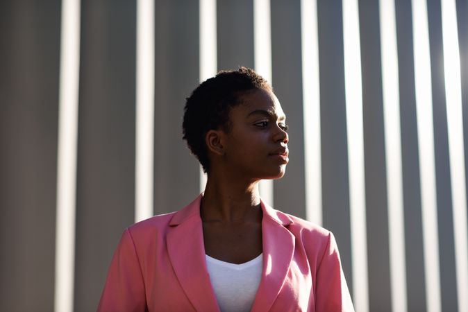 Female wearing suit with pink jacket outside office with striped shadows looking to her side