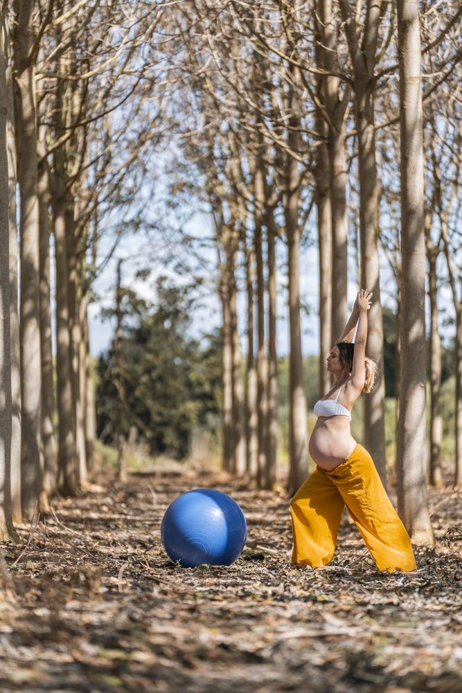 Adult pregnant woman training with pilates ball in park during sunny day
