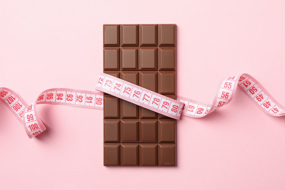 Measuring tape and chocolate bar on pink background