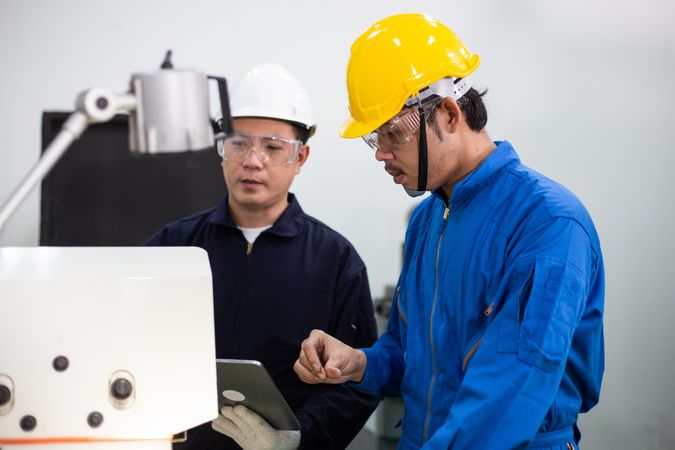 Asian men in blue jumpsuits and hard hats working in manufacturing