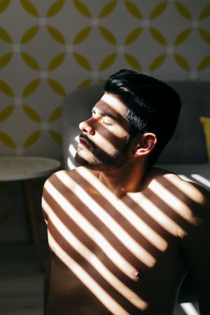 Young naked man covering sunlight with hand