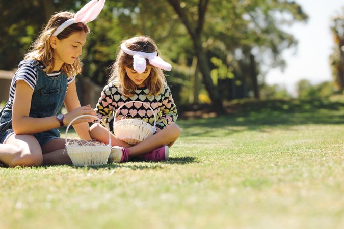 Two girls wearing rabbit ear headband playing in the backyard with baskets