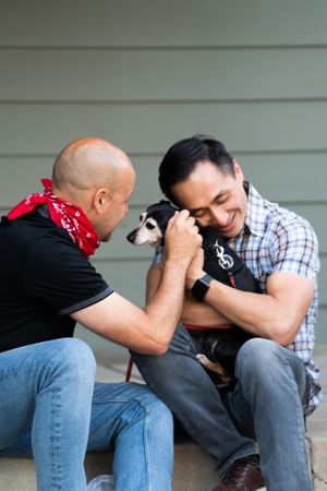 Man snuggling up to his dog and smiling with his eyes closed while his partner pets the dog