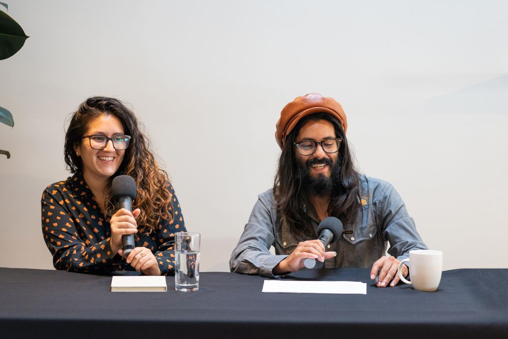 Man and woman smiling address the room on a panel