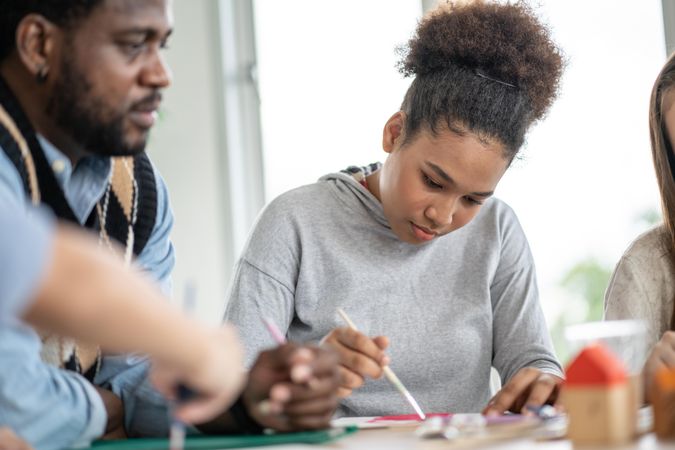 Black teenage student painting in class with male teacher