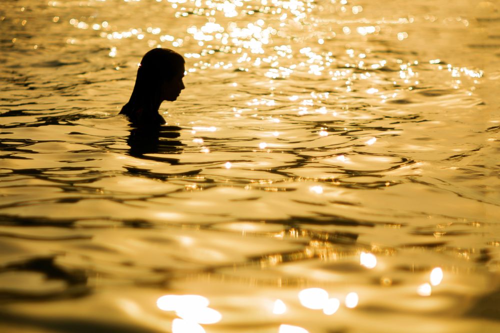 Anonymous woman standing in sea in sunset