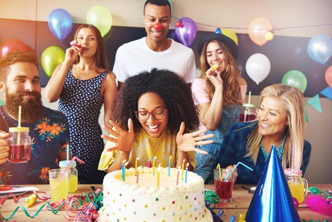 Happy woman surrounded by her friends as she blows out her birthday candles