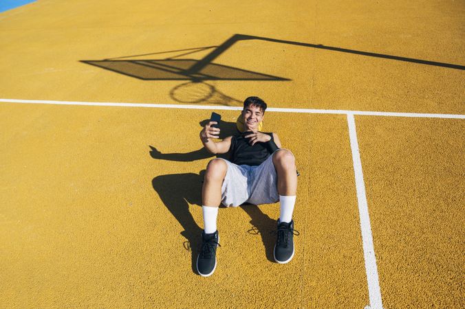 Male basketball player using his smartphone resting after training