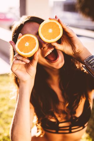 Woman holds orange halves up to her eyes while smiling