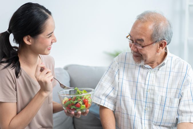 Mature man smiling while eating delicious healthy salad from beloved daughter