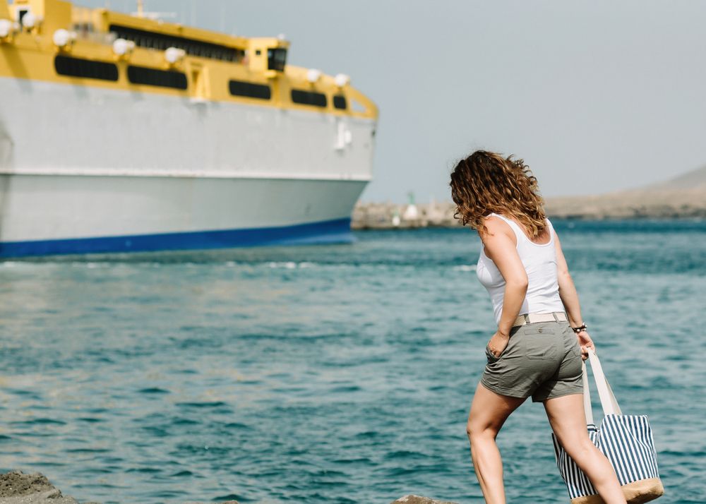Curly woman looking at ship in water on seashore