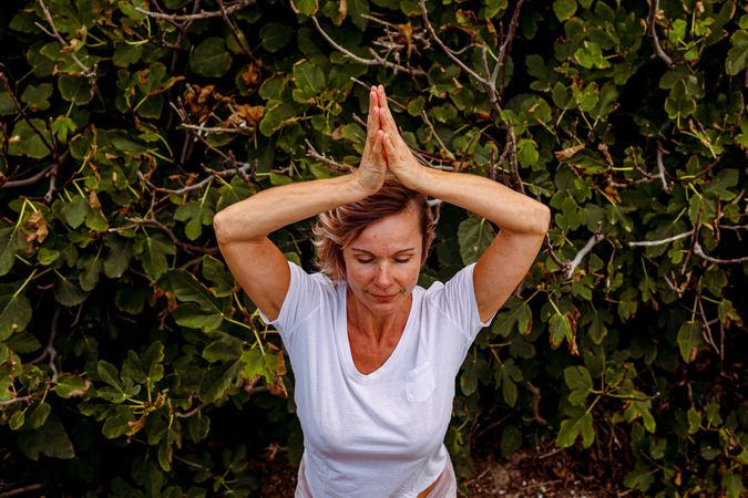 Adult woman meditating near bush