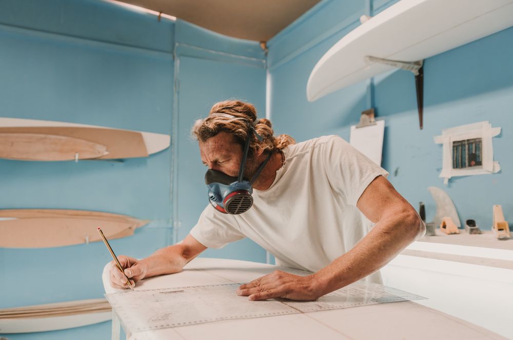 Man in respirator measuring surf board in workshop
