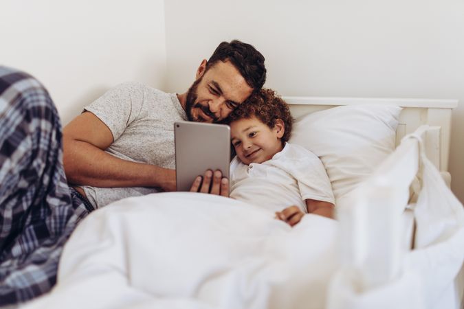 Father and son lying on bed watching a movie on tablet pc
