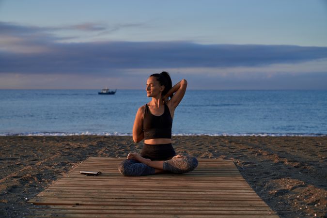 Hispanic woman practicing Cow face asana on beach