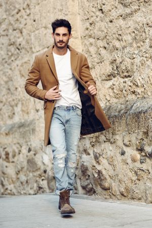 Man walking past Spanish wall in jacket and jeans