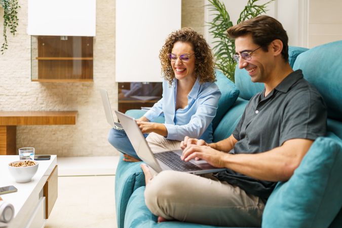 Cheerful couple sitting on couch while working on laptop in living room