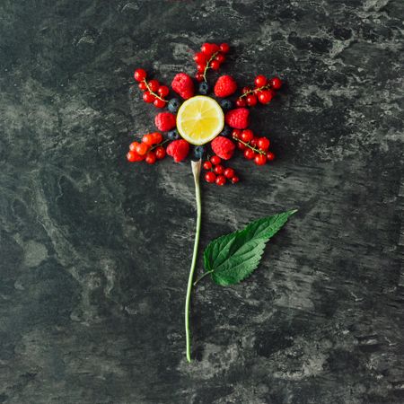 Red flower of red healthy food, fruits, and vegetables with green leaves on dark stone background