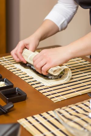 Hands of female chef rolling up a Japanese sushi with traditional mat, vertical