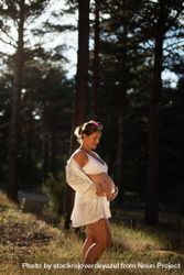 A pregnant woman caresses her belly and her future child wearing a silk robe in the park 0yXXEG
