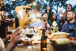 Group of people drinking and singing around the bbq food table drinking wine and beers and making lights with smart phones torches