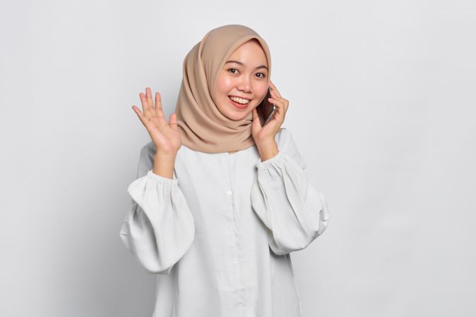 Happy Asian Muslim woman talking on cell phone and waving