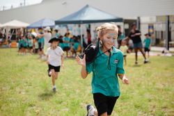 Girl in green polo shirt and dark pants running on grass field