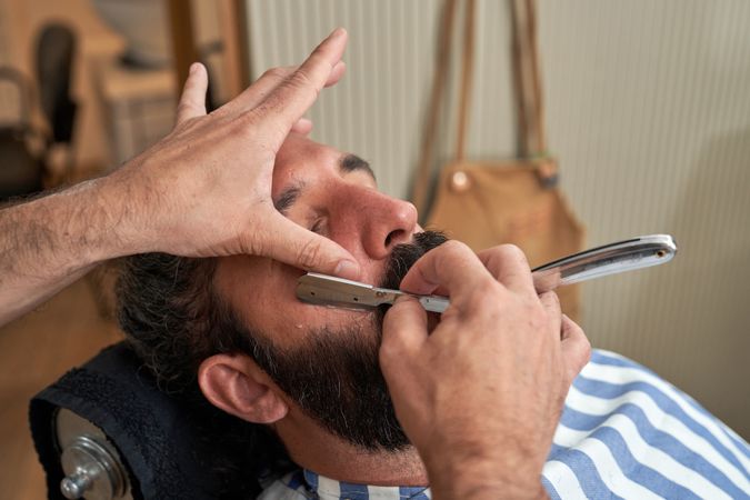 Crop barber cutting beard of client