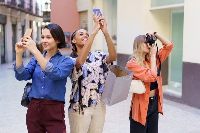 Three smiling women looking up and taking pictures with their phone in lane