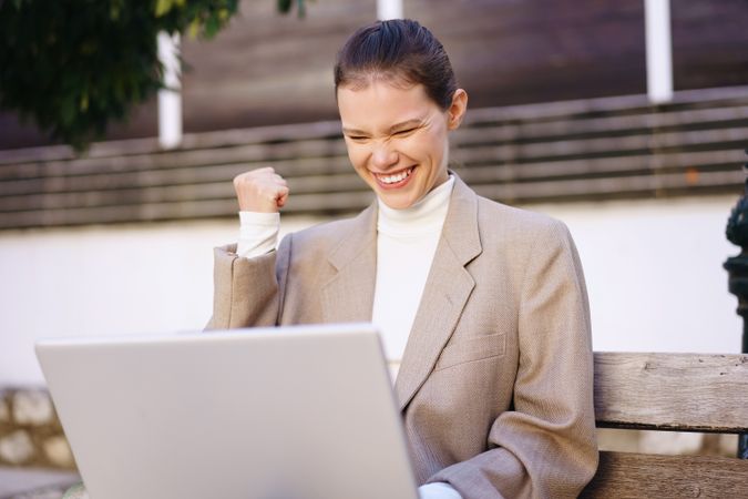 A woman joyfully celebrating her success while confidently working outdoors on her laptop