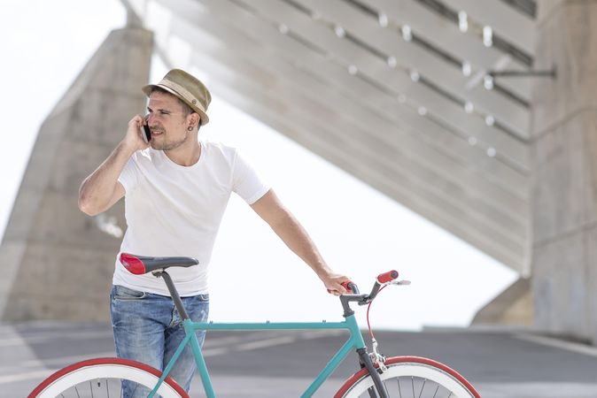 Male with bicycle talking on phone under modern building