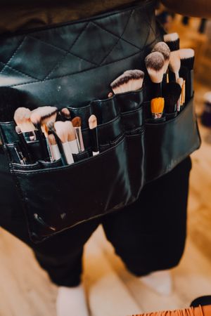 Unrecognizable makeup artist with brushes in apron bag