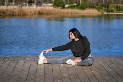 a young sportswoman stretches while sitting on a lake jetty