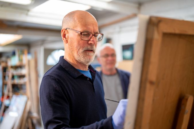 Male artist painting with man behind him