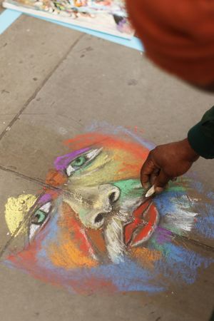 Person drawing face on sidewalk floor with colorful chalks in London, UK 