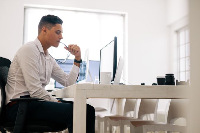 Man holding eyeglasses working on computer in office with a coffee cup on the table