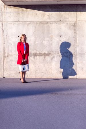 Businesswoman wearing red jacket and handbag standing in the street with long shadow