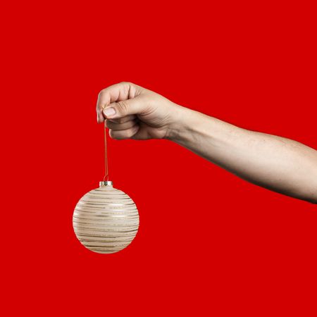 Hand holding a Christmas bauble decoration on a red background.