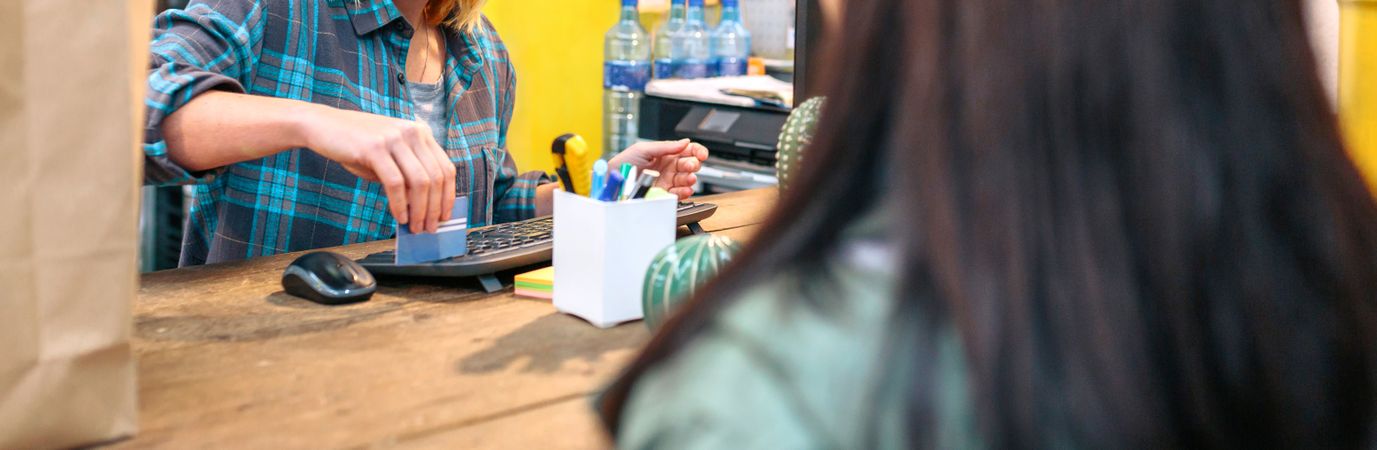 Banner of female cashier passing credit card through store terminal to charge customer purchase