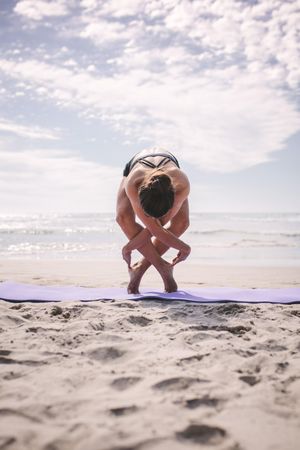 Fit woman doing yoga exercise at the beach on a sunny day