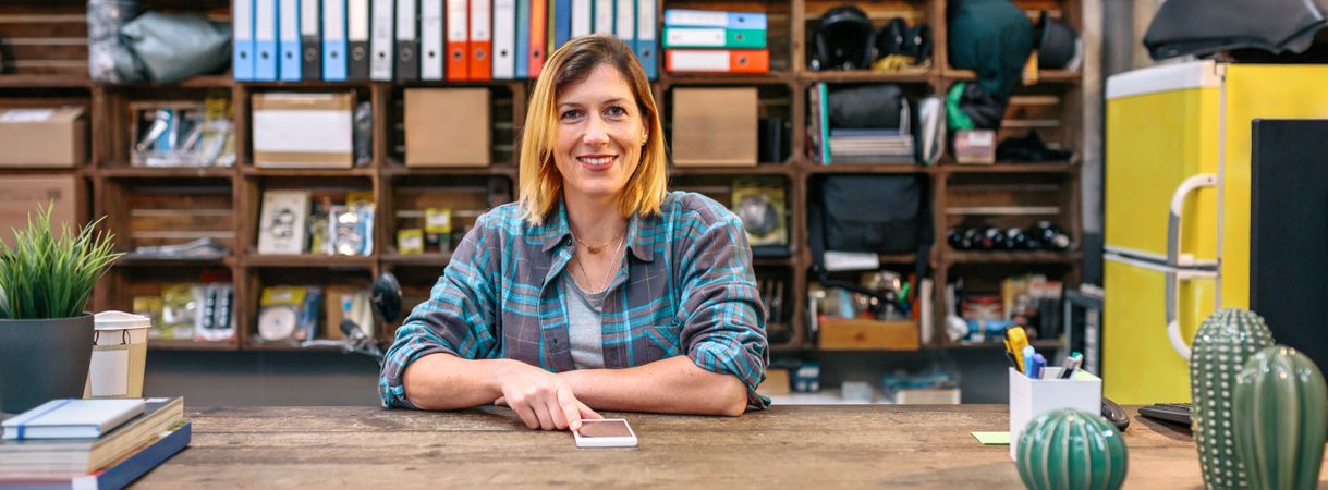 Banner of smiling blonde young female employee looking at camera behind of industrial shop counter