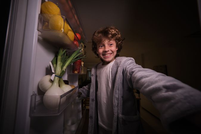 Joyful boy standing near opened fridge